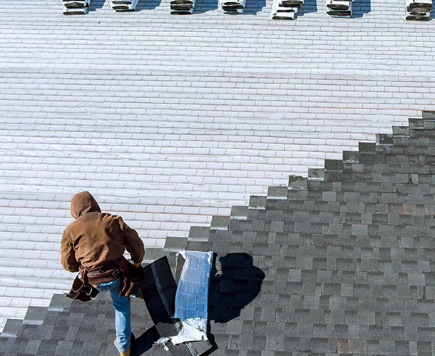 Roofer working on shingle roof maintenance, replacing dark shingles with light ones.